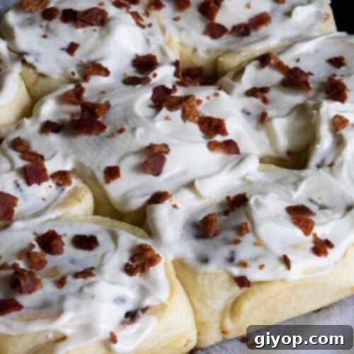 Maple bacon cinnamon rolls on a parchment paper lined wooden board.