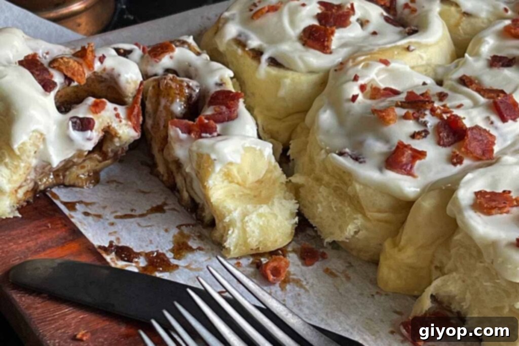 A perfectly sliced maple bacon cinnamon roll revealing its gooey, layered interior with crispy bacon bits.
