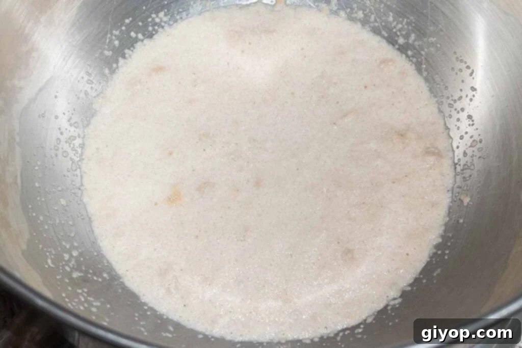 Instant dry yeast actively blooming in a bowl of warm milk and sugar, forming a bubbly layer on top.