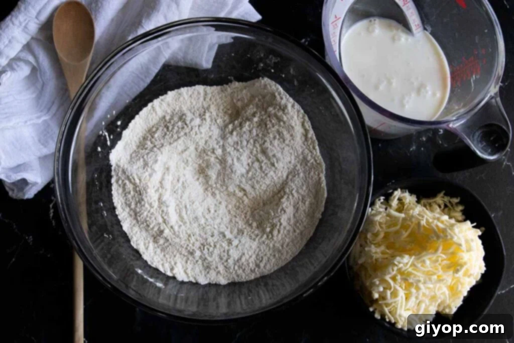 Dry ingredients in a glass mixing bowl, buttermilk in a measuring cup, frozen grated butter in a small black bowl, ready for mixing.