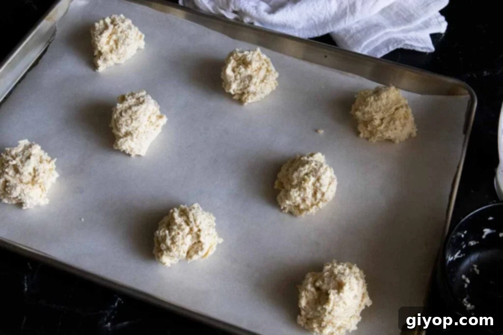 Biscuit dough dropped onto a parchment-lined baking sheet, ready for the oven.