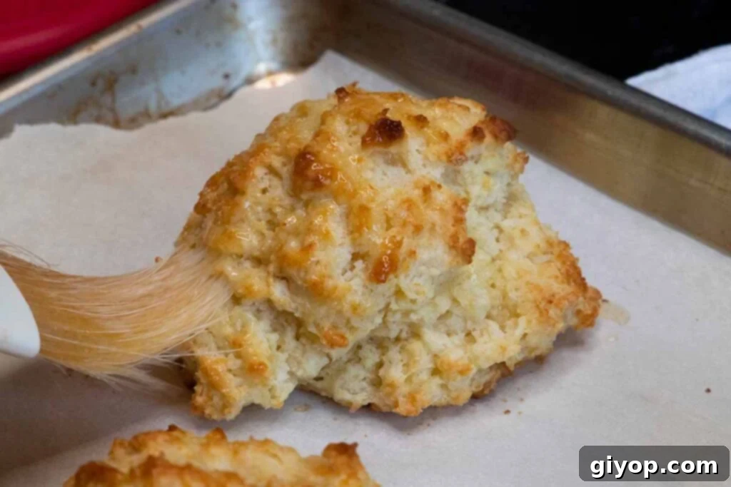 A warm, golden buttermilk drop biscuit being brushed with melted butter, straight from the oven.