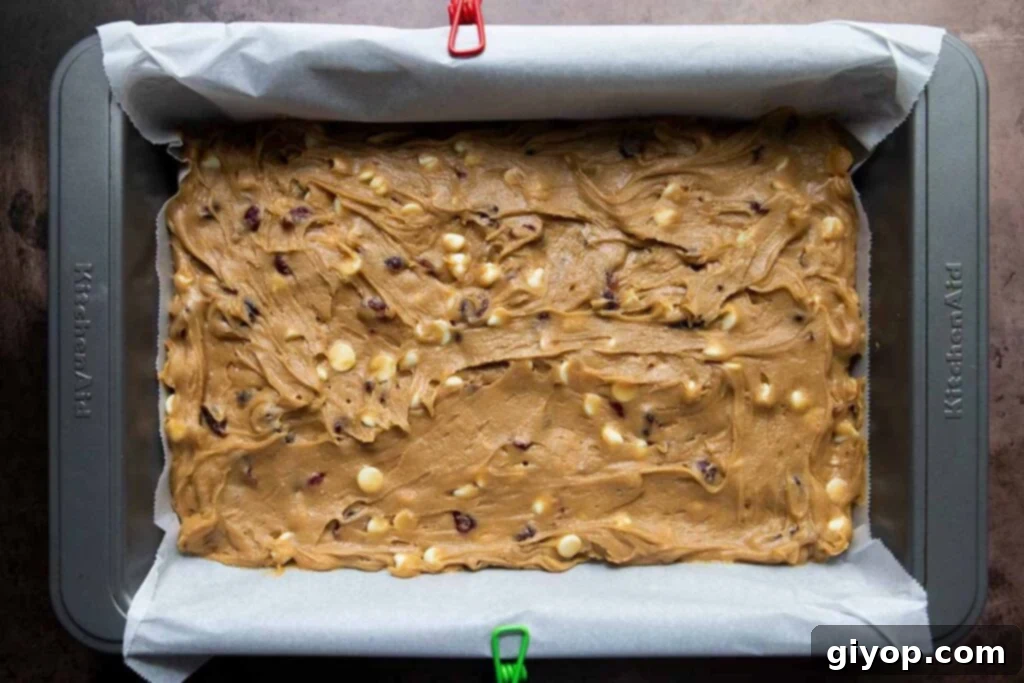 Smooth blondie dough spread evenly into a parchment-lined baking pan, ready for the oven.