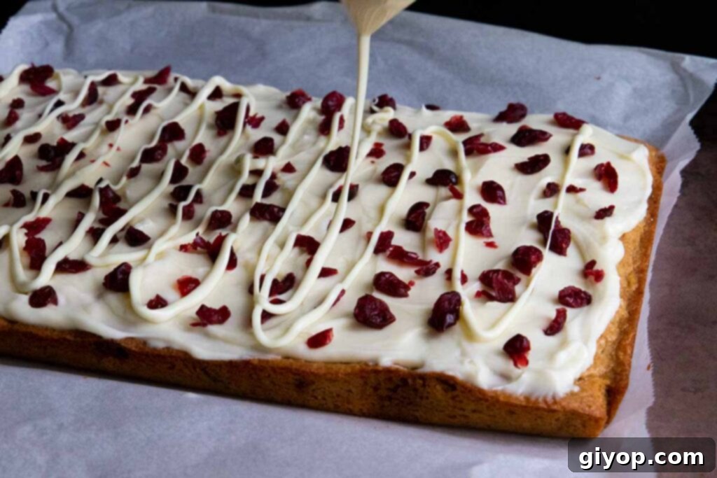 Melted white chocolate being drizzled in an artistic pattern over the frosted cranberry bliss bars.