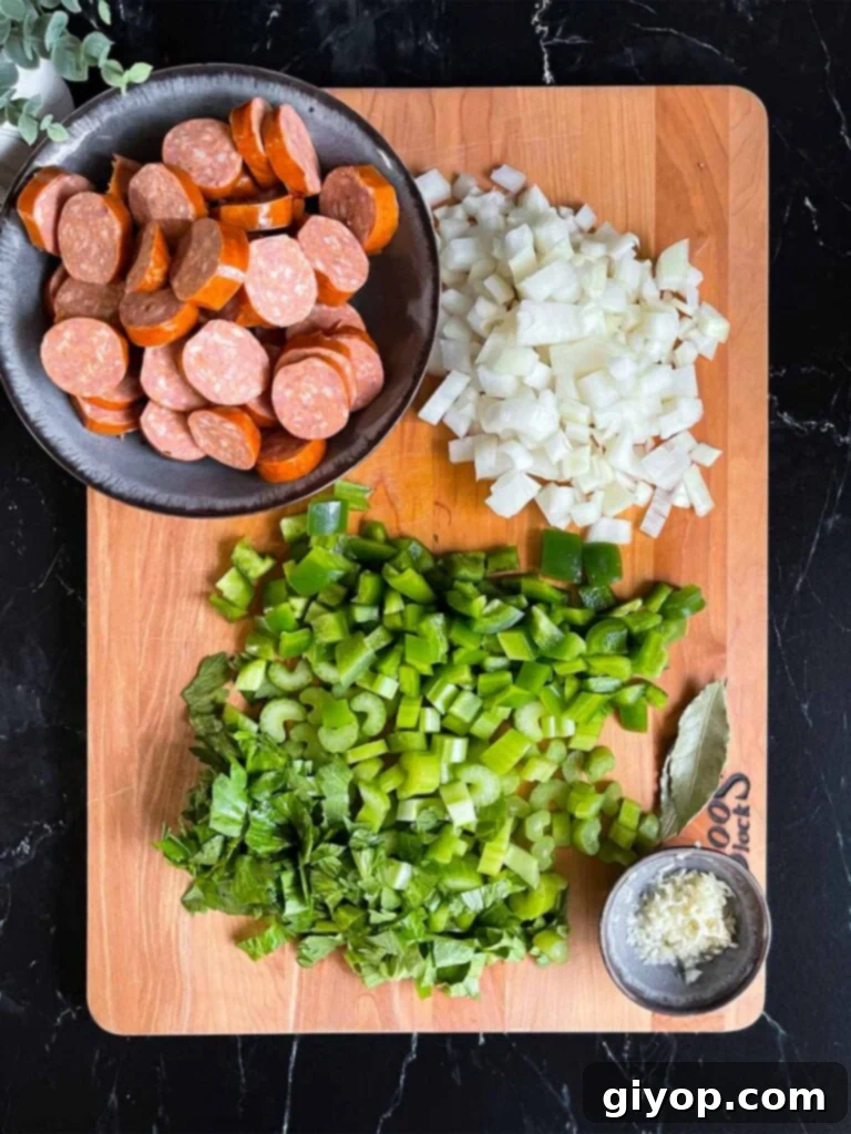 Soulful Slow Cooker Red Beans and Rice 6 Sliced andouille, onions, green bell pepper, celery, minced garlic and bay leave on a wooden cutting board.