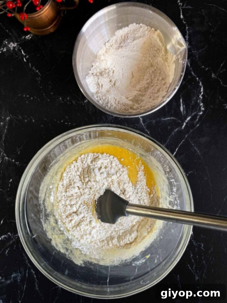 Dry ingredients being added to the wet ingredients for cranberry pistachio biscotti in a glass bowl.