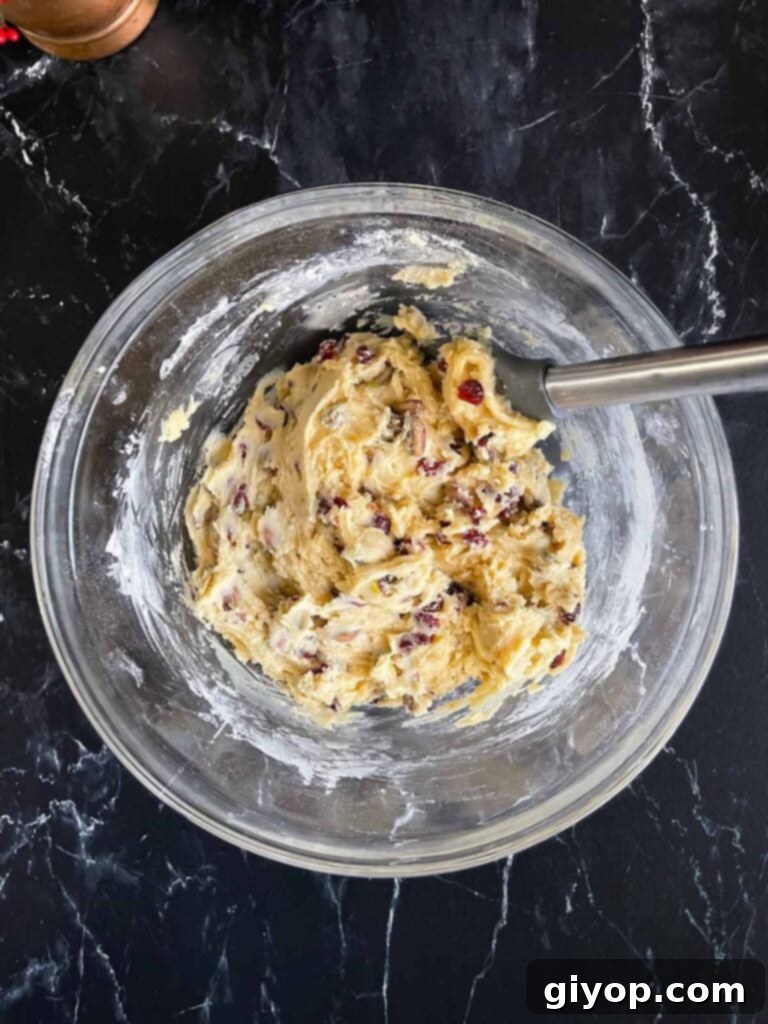 Cranberry pistachio biscotti dough mixed in a glass mixing bowl on a dark surface, showing the vibrant cranberries and green pistachios.