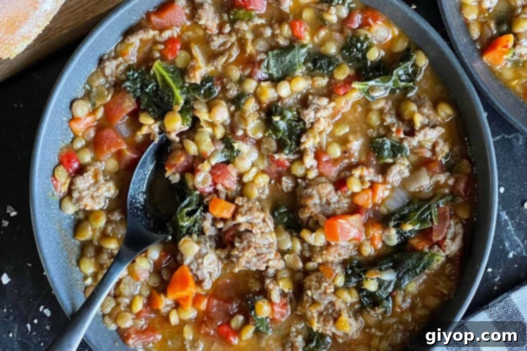 Lentil soup with sausage and spinach in a dark bowl.