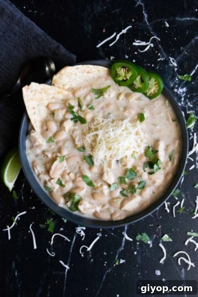 A close-up view of creamy white chicken chili served in a dark bowl, highlighting the tender chicken pieces, cannellini beans, and rich texture.