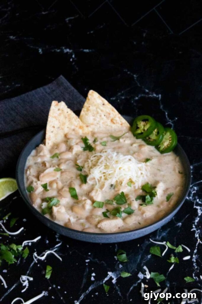 White chicken chili in a black bowl garnished with vibrant sliced jalapeños and fresh green cilantro, showcasing its appetizing appeal.