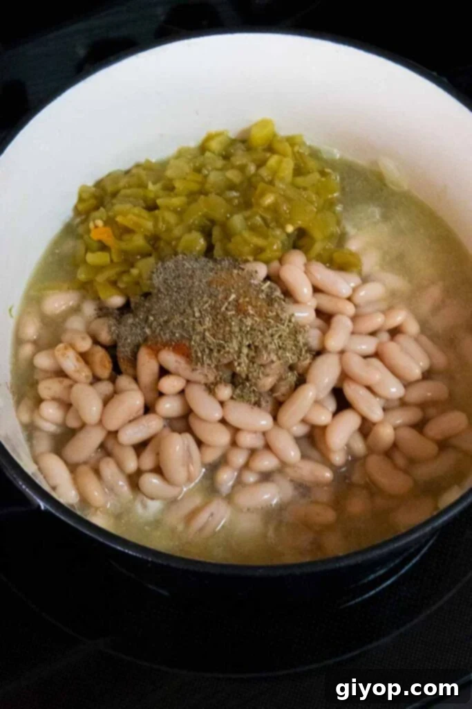 A large Dutch oven filled with raw and partially cooked ingredients for white chicken chili, including chicken, beans, onions, and spices, before simmering.