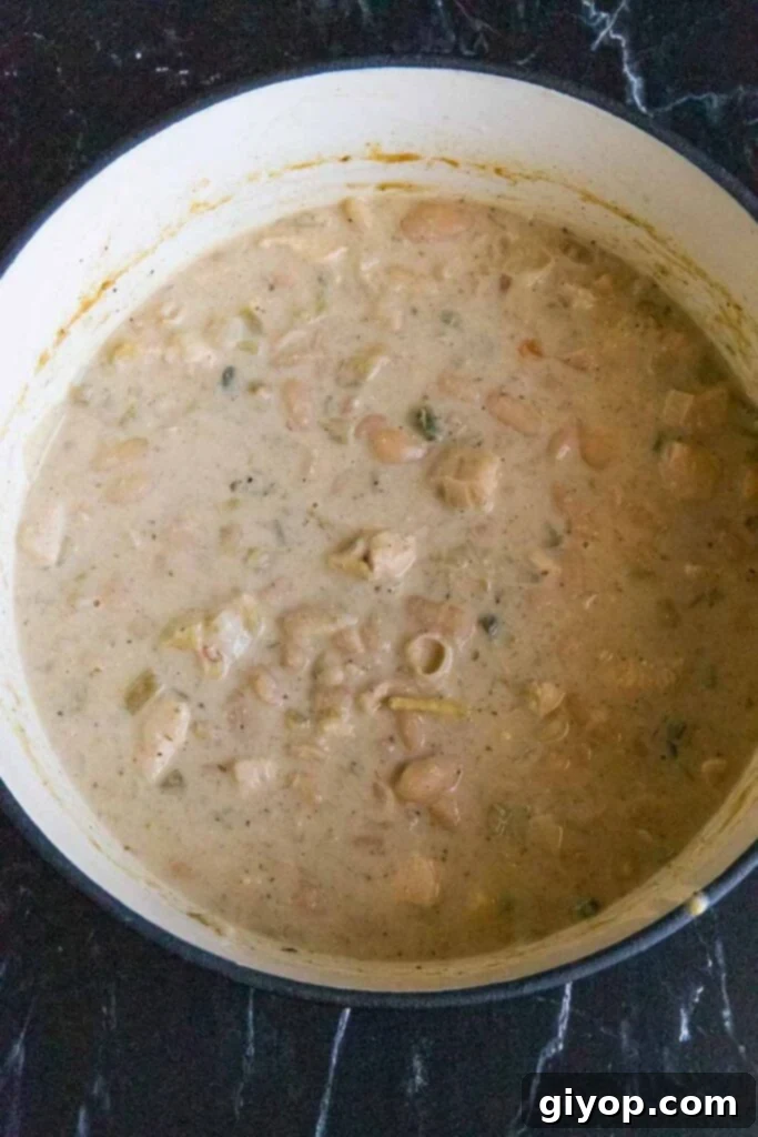 Cooked white chicken chili simmering gently in a large Dutch oven, indicating a rich, thick texture and deep flavors developing.