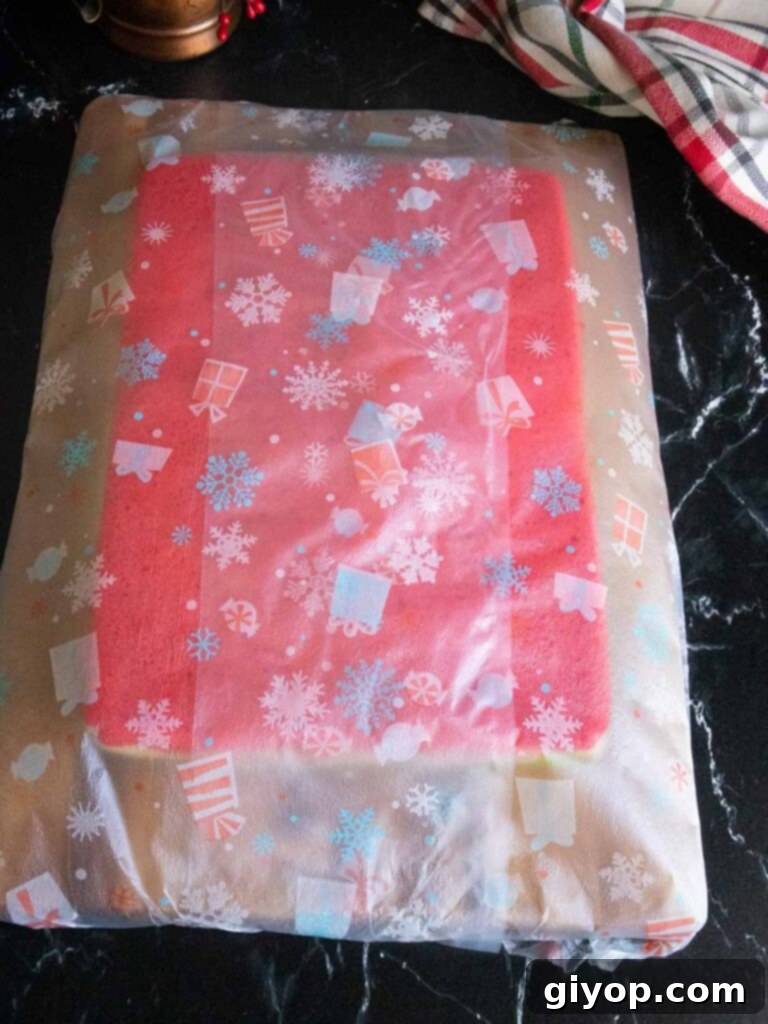 The stacked cookie layers on a wooden board wrapped in plastic wrap.