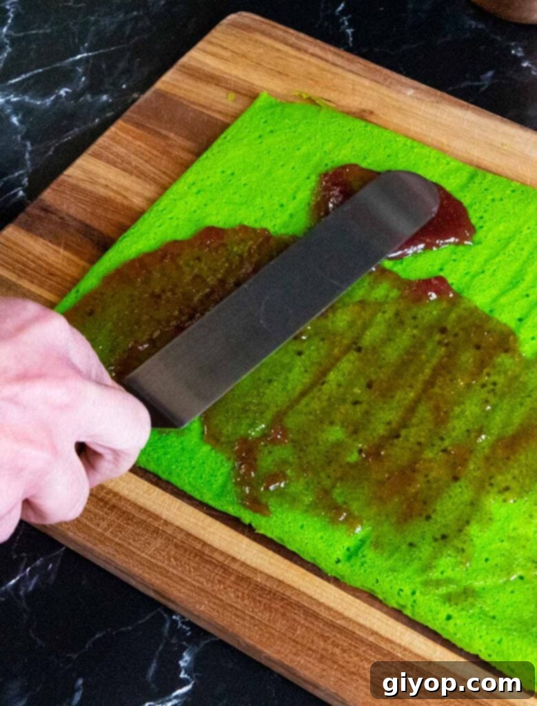 Raspberry jam being spread on the green cookie layer.