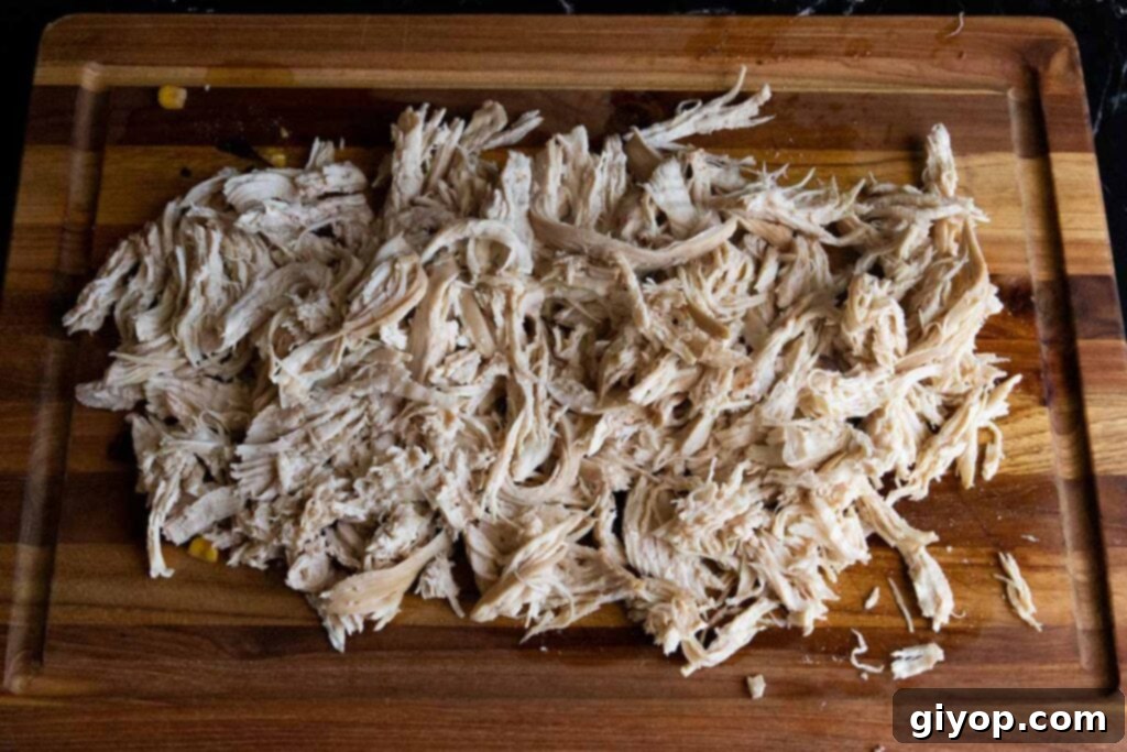 Comforting Stovetop Chicken Tortilla Soup 5 Perfectly cooked and shredded chicken on a wooden cutting board, ready to be added back to the soup.