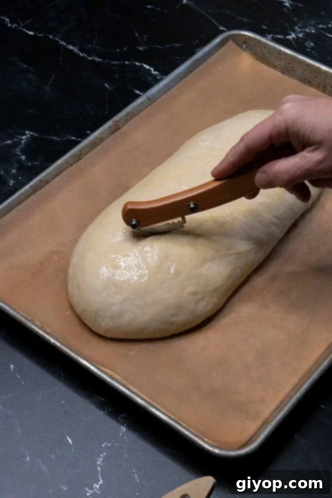Cutting diagonal slices into an unbaked loaf of Italian bread with a sharp knife.