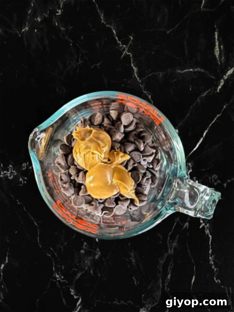 Peanut butter and chocolate chips in a small glass measuring cup on a dark surface, prepared for melting.