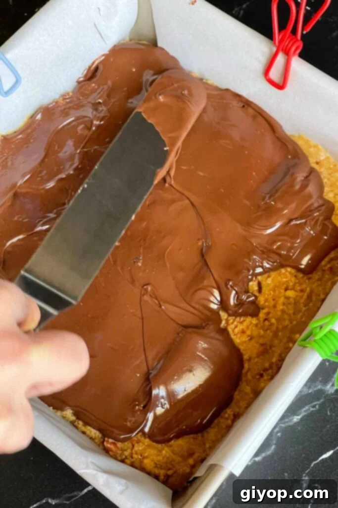 Melted chocolate being spread evenly over the top of the peanut butter pretzel bars' base.