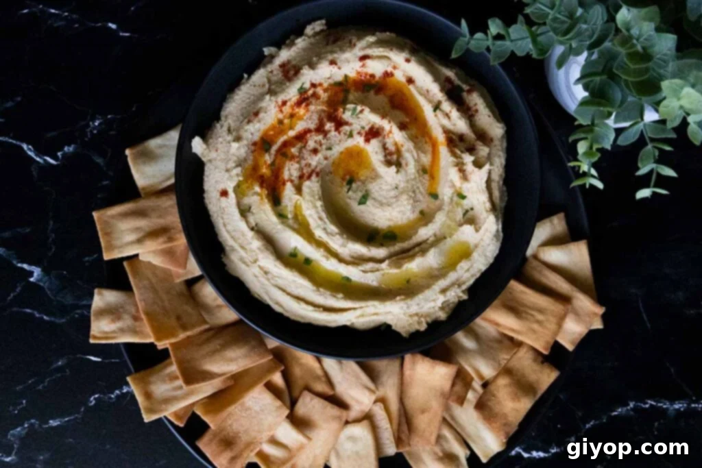 Homemade hummus in a black bowl surrounded by crispy pita chips, garnished with a drizzle of olive oil and a sprinkle of paprika.