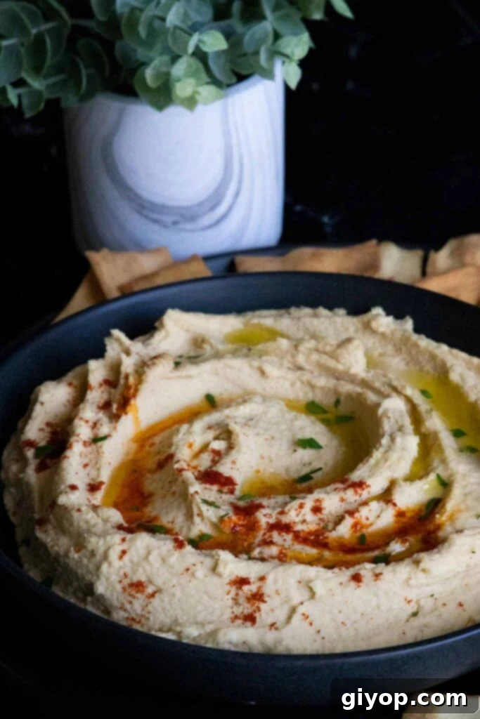 Close-up of homemade hummus in a black bowl, garnished and ready to serve with pita chips scattered around.