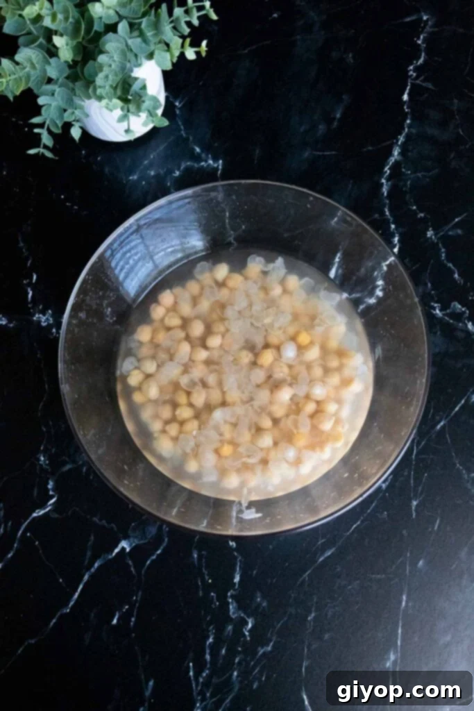 Chickpeas soaking in hot water in a clear glass bowl, illustrating the first step of the skinning process.