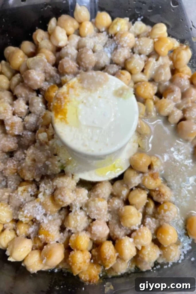 All the hummus ingredients, including chickpeas, garlic, lemon, tahini, and olive oil, in the bowl of a food processor before blending.