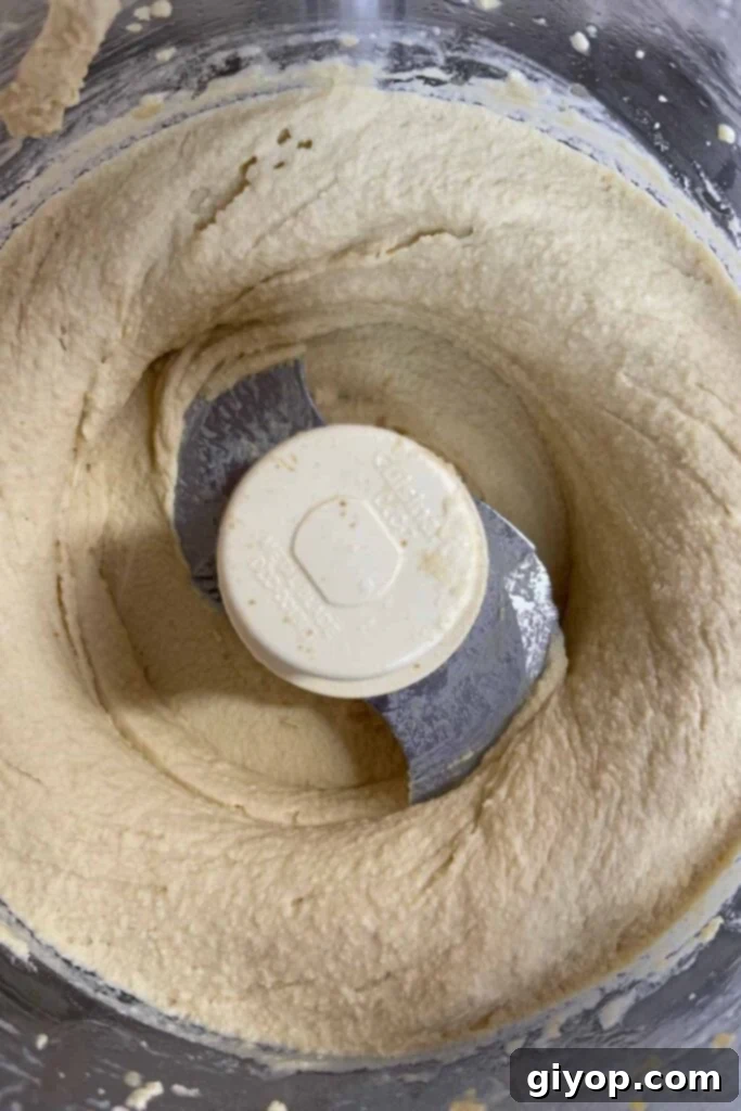 Creamy pureed hummus in the bowl of a food processor after blending, ready for final adjustments.