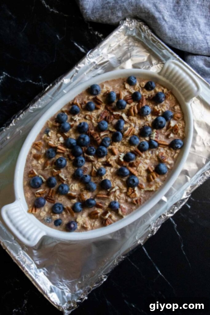 Wholesome Blueberry Baked Oatmeal 6 An unbaked blueberry oatmeal casserole, beautifully topped with extra blueberries and pecans, resting on a foil-lined baking sheet, prepared and ready to go into the oven.