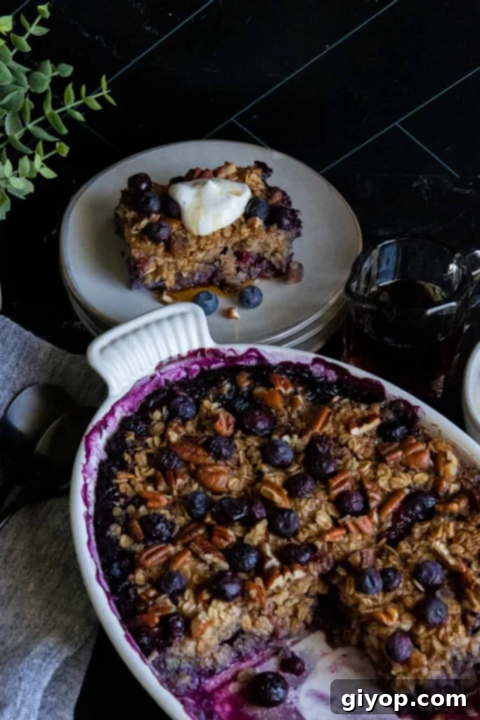 Wholesome Blueberry Baked Oatmeal 8 A perfectly portioned serving of blueberry baked oatmeal on a gray plate, with the remainder of the casserole still in the oval baking dish, highlighting its comforting and ready-to-eat texture.
