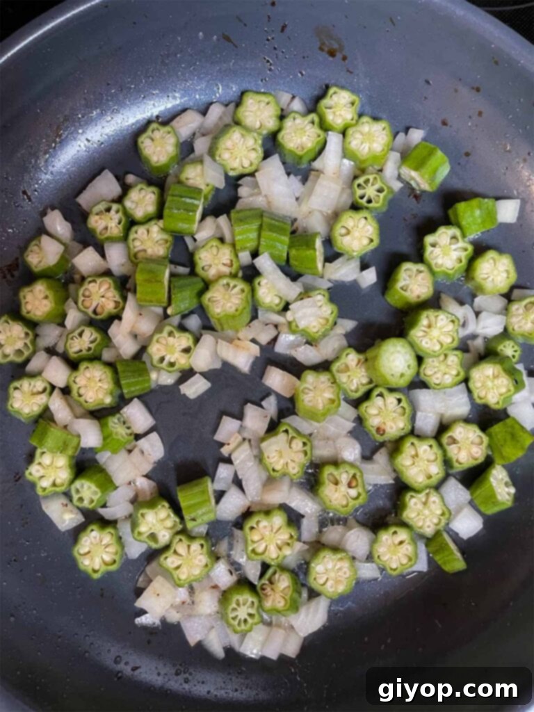 Diced sweet onions and fresh okra sautéing in a large cast-iron skillet, forming the flavorful base for the summer succotash.