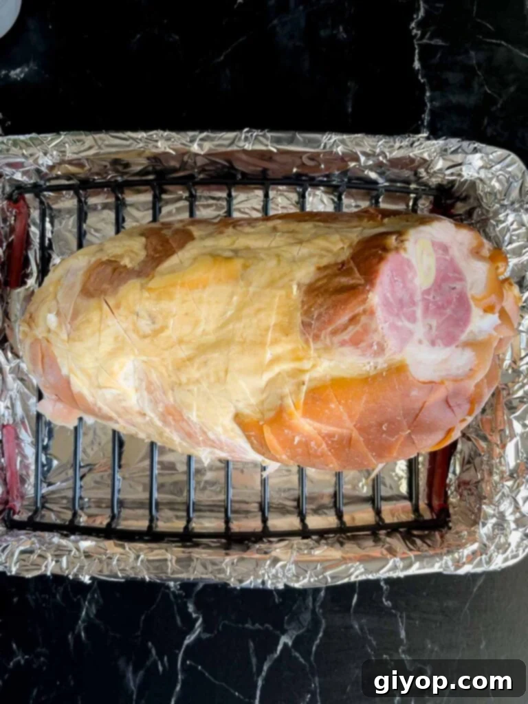 Prepared ham placed on a rack inside a foil lined roasting pan on top of a rack inside a foil lined roasting pan.