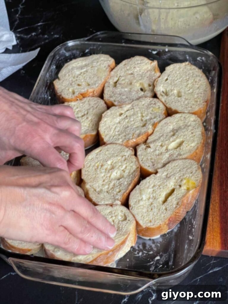 A hand dipping a thick slice of bread into a bowl of egg custard, preparing it for baking.