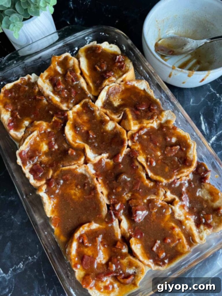 A rich topping of melted butter, brown sugar, maple syrup, and crumbled bacon being poured over the soaked French toast, ready for baking.