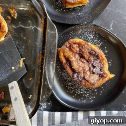 Individual servings of golden brown Overnight Maple Bacon Baked French Toast, garnished with powdered sugar on black plates.