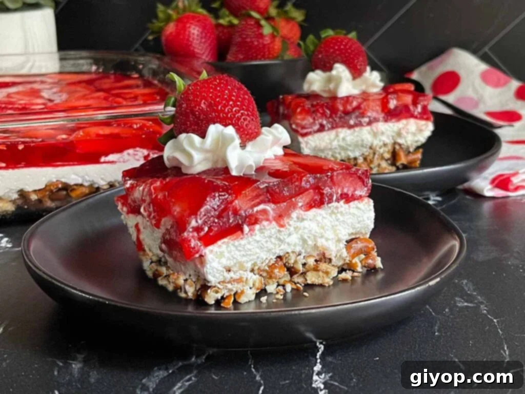 A perfectly sliced serving of Strawberry Pretzel Salad on elegant black plates, garnished with a dollop of whipped cream and a fresh strawberry.