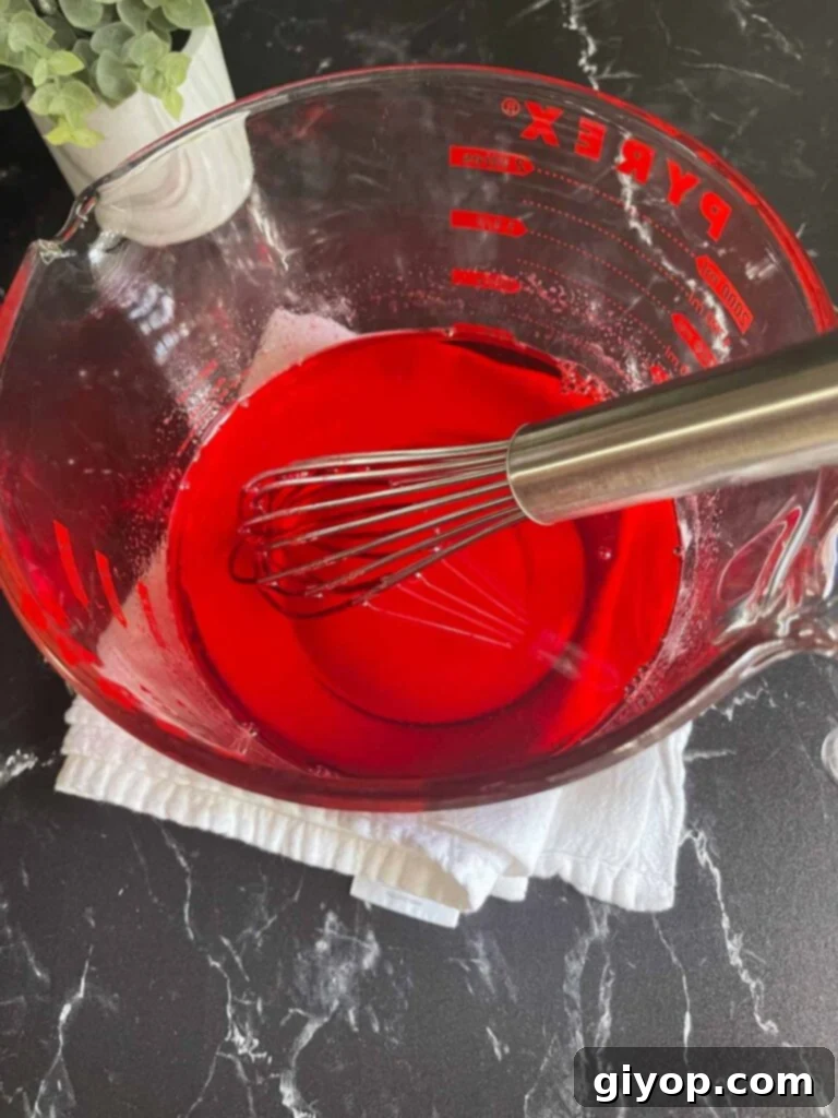 Strawberry jello mixture cooling in a large measuring cup.