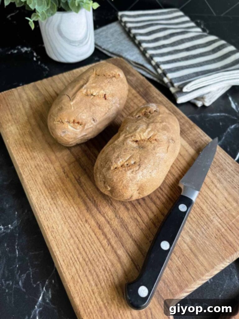 Two baked russet potatoes cooling on a cutting board, ready for preparation.