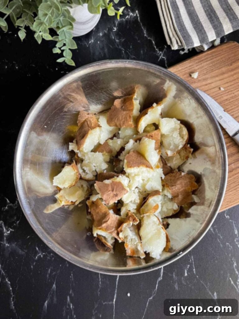 Hand-broken baked potato pieces in a metal bowl, showing irregular shapes for maximum crispiness.