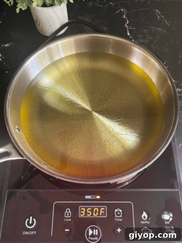 Vegetable oil heating to medium-high in a large steel skillet, preparing for frying.