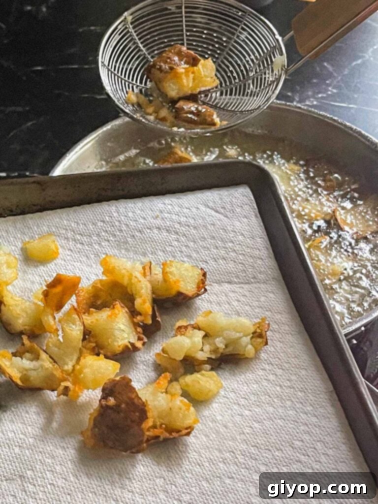 Golden-brown fried potato bites being carefully removed from hot oil with a slotted spoon.