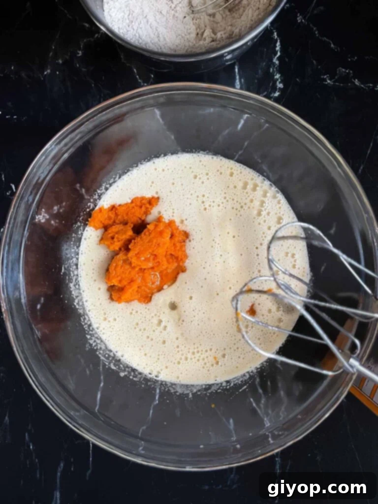 Pumpkin puree and vegetable oil added to the wet ingredients in a glass bowl.