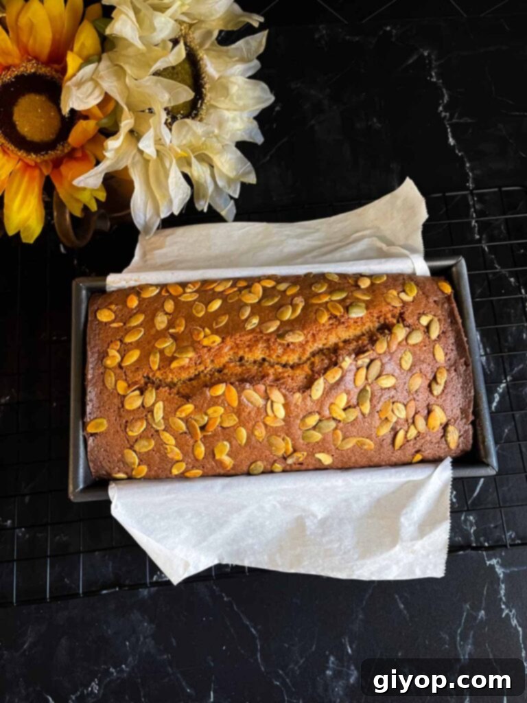 Baked pumpkin bread in a loaf pan on a dark surface.