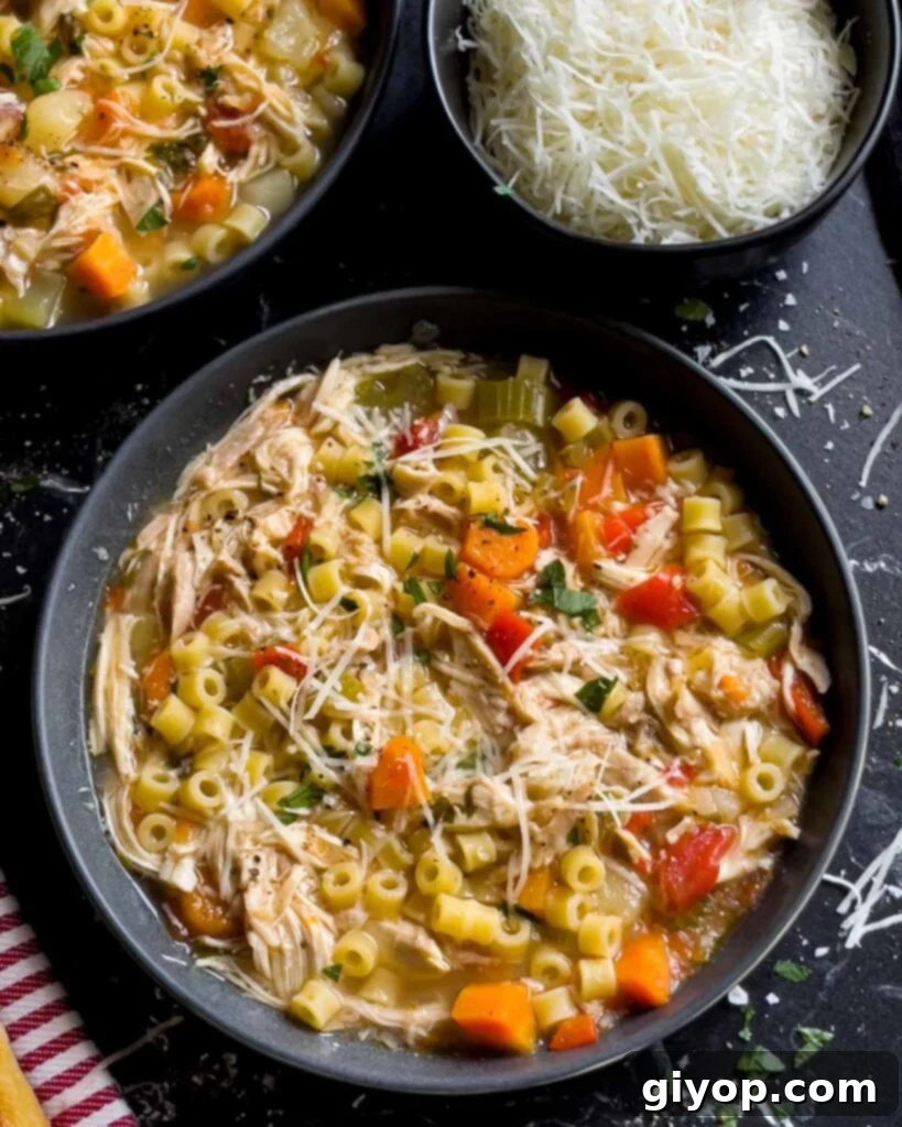 Sicilian chicken noodle soup in a dark bowl garnished with fresh parsley and Pecorino Romano cheese.