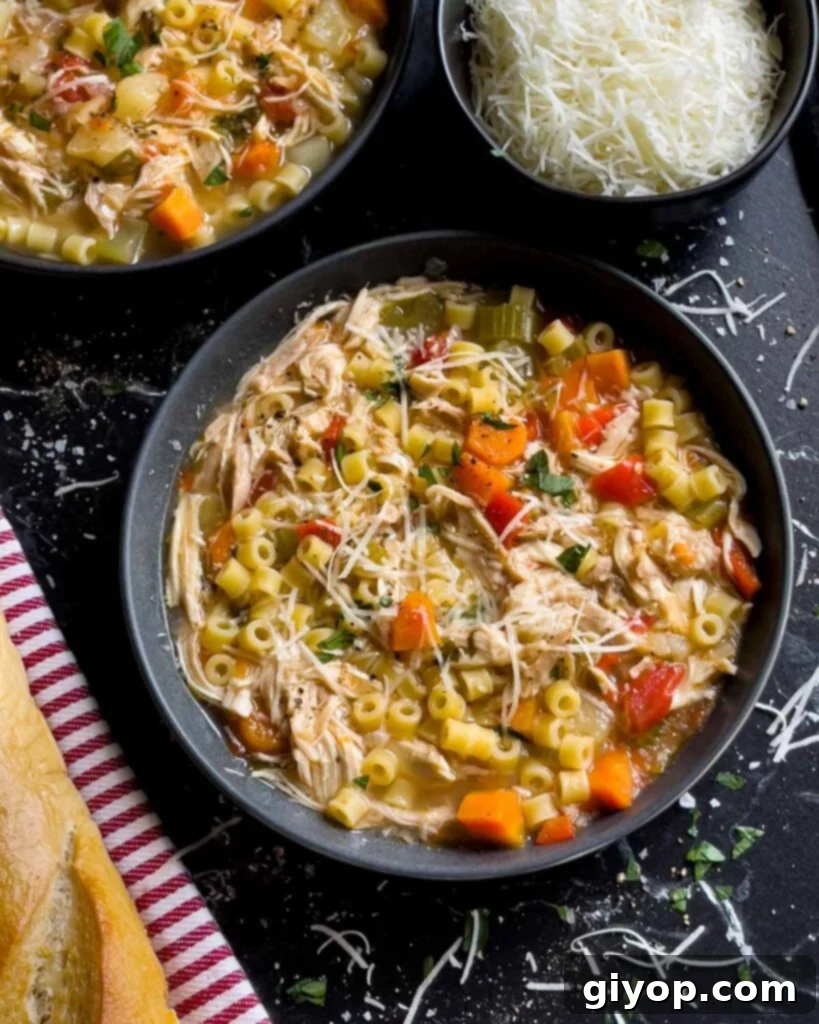 Sicilian chicken noodle soup in a dark bowl garnished with fresh parsley and Pecorino Romano cheese.
