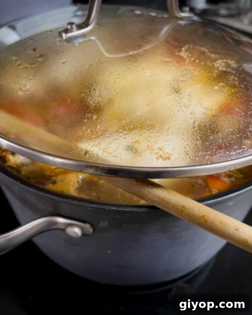 Sicilian chicken noodle soup simmering with the lid propped slightly open using a wooden spoon.