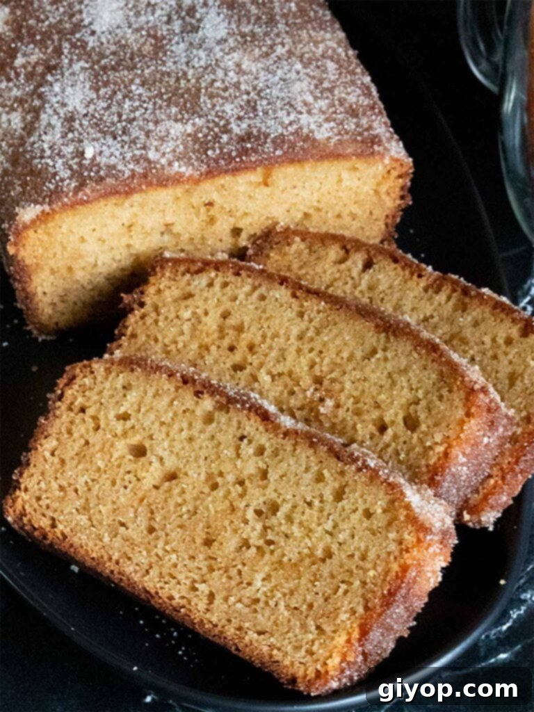 Apple cider doughnut loaf cake sliced on a black platter, showing its moist interior and spiced topping.