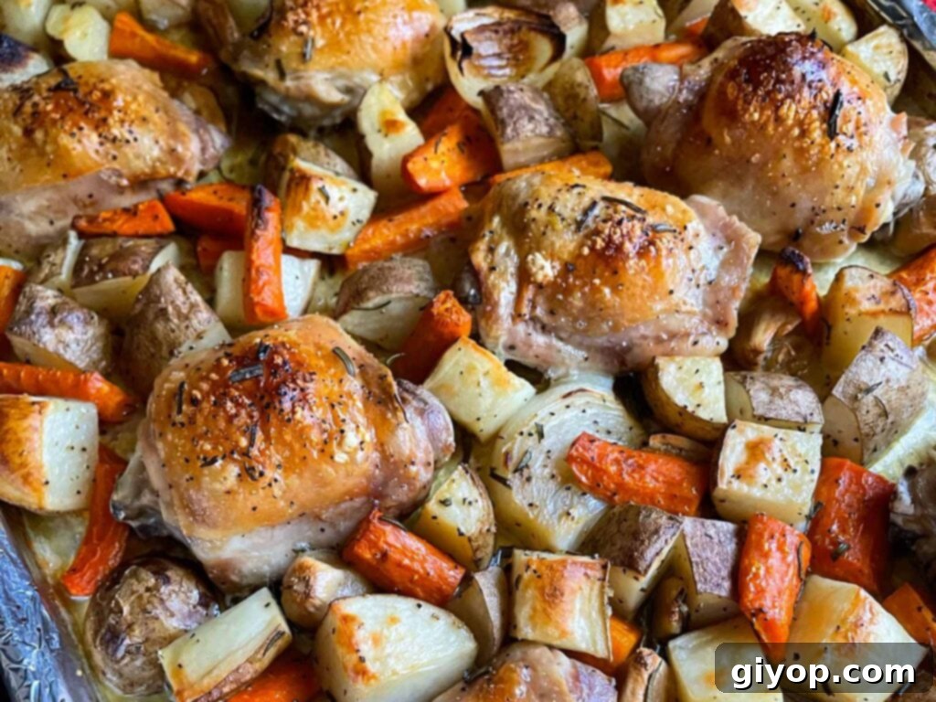 Golden brown one-pan roasted chicken thighs, crispy potatoes, and caramelized carrots on a foil and parchment paper lined baking sheet, ready to serve.