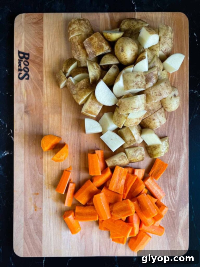 Uniformly cut raw potatoes and carrots on a wooden cutting board, ready for roasting.