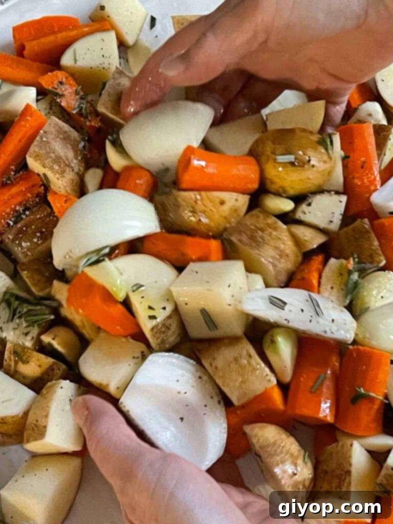 Raw chicken thighs, potatoes, carrots, onions, and whole garlic cloves expertly tossed in olive oil and seasonings on a lined baking sheet.
