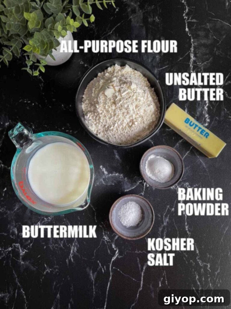 A flat lay photograph showcasing the key ingredients for butter swim biscuits: flour, butter, buttermilk, baking powder, and kosher salt, arranged neatly on a black marble countertop.